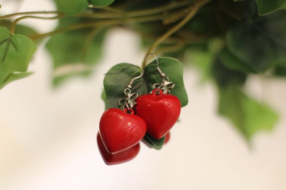 Red heart-shaped earrings hanging from green leaves.