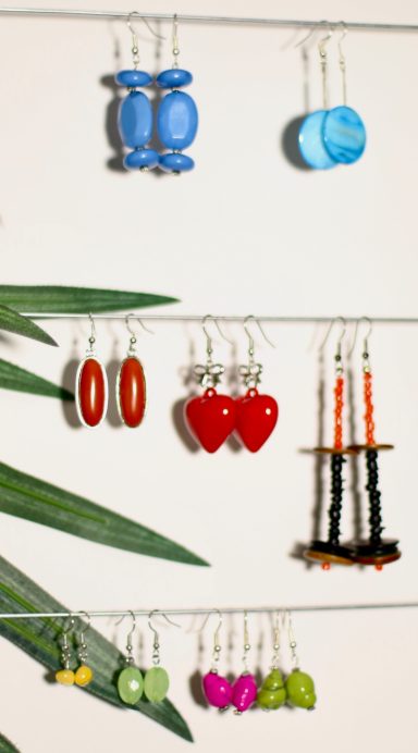 Colorful earrings displayed on strings against a neutral background with greenery.