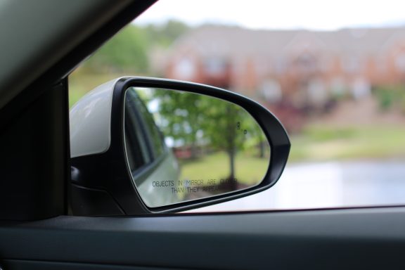 Side mirror view of a car reflecting a tree and buildings in the background.