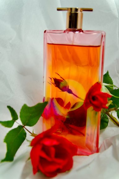 Pink perfume bottle with a floral design, surrounded by red roses and green leaves.