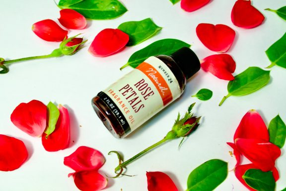 Brown bottle labeled "Rose Petals" surrounded by red rose petals and green leaves.